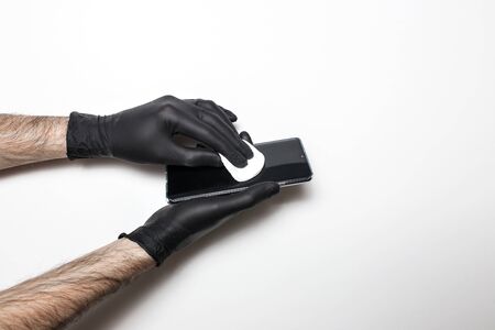 Male hands in black medical gloves disinfect the phone screen. White isolated background.の写真素材