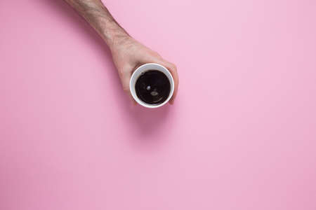 A male hand reaches for a glass with a coffee on a pink background. View from above.の写真素材