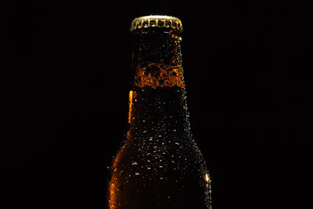 Bottle of beer with drops of water close-up on a black isolated background.