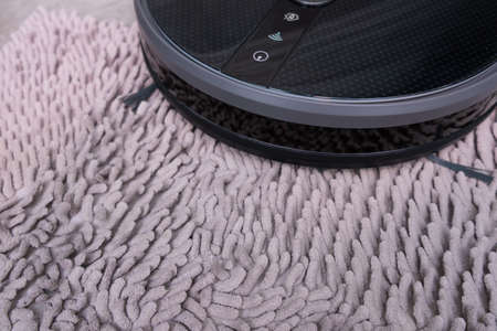 Robot vacuum cleaner on a gray carpet with a large pile close-up.の写真素材