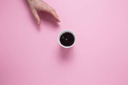 A male hand reaches for a glass with a coffee on a pink background. View from above.の写真素材
