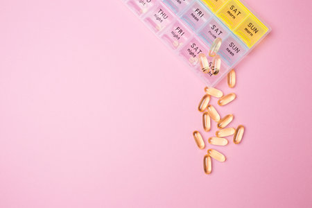 Organizer for medical pills on a pink isolated background close-up. Organization of taking pills of the day. Transparent vitamins lie nearby.の写真素材
