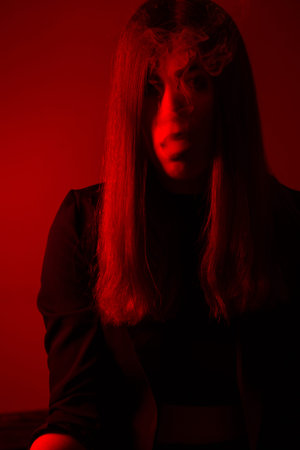 Girl model smokes vape in red light.