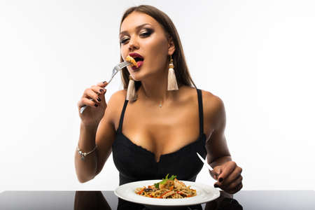 Sexy girl at an even table with a fork and knife in her hands. On the table there is a plate with noodles and shrimps.の写真素材