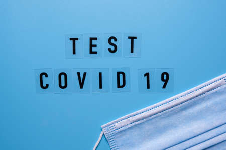 The word COVID test and a medical mask on a blue background top view.の写真素材