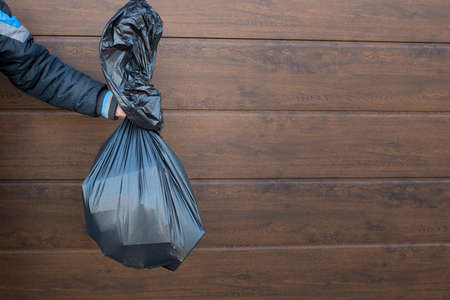 The guy holds a black trash bag close-up.の写真素材