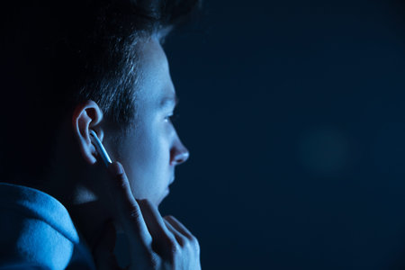 Young guy with wireless headphones in the studio on a black background in neon light.