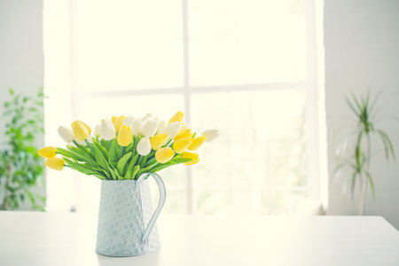 A bouquet of tulips in a pot in the form of a teapot on a white table. Taken in warm daylight.
