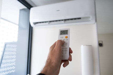 A mans hand holds a remote control from an air conditioner with a temperature on the screen of 21.