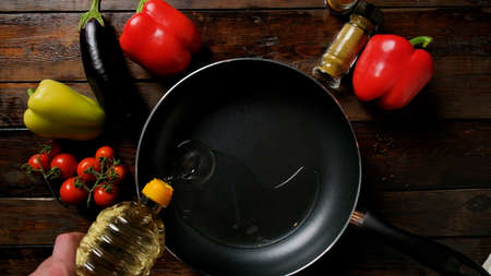 Sunflower oil is poured into a frying pan, top view. Wooden table on which spices lie vegetables.の写真素材