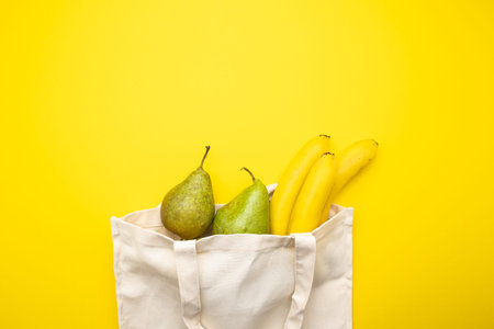 Eco bag with bananas and pears on a yellow background top view.