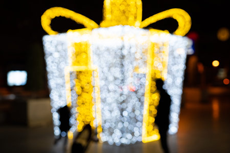 Blurred photo of a large Christmas gift decorated with garlands on the street.