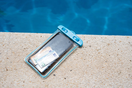 Waterproof case with money and a smartphone on the background of the pool on a sunny summer day.