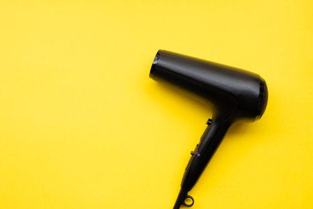 Black hair dryer on blue and yellow paper backgroundの写真素材
