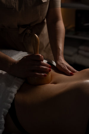 Anti-cellulite massage on the stomach using wooden objects. Massage salon in a dark room.の写真素材
