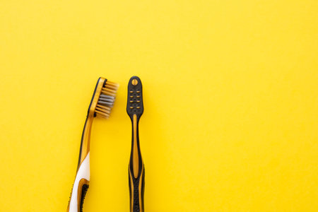 Two black and yellow toothbrushes on a bright yellow background.