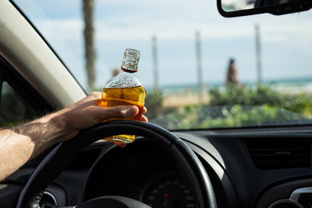 Driver driving a car with a bottle of alcohol in his hands close-up.の写真素材