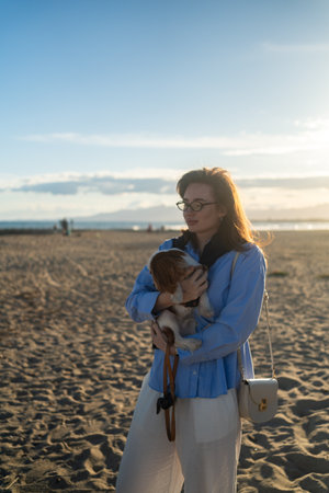 A young woman hugs her puppy on the beach at sunset. Warm light, waves, and smiles capture a peaceful, joyful moment of connection and relaxation.の写真素材