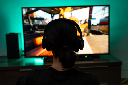 Young guy gamer in headphones plays on the console close-up rear view.