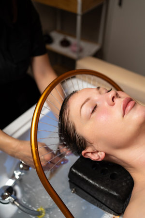 Woman enjoying a rejuvenating head spa and scalp treatment with continuous water flow in a salon. Feeling relaxation and wellnessの写真素材
