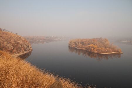 A small island as if floating in the middle of a river, shrouded in morning fogの写真素材