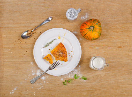 A piece of pumpkin pie in a bowl, pumpkin, fork, powdered sugar, nuts, milk, on wooden table