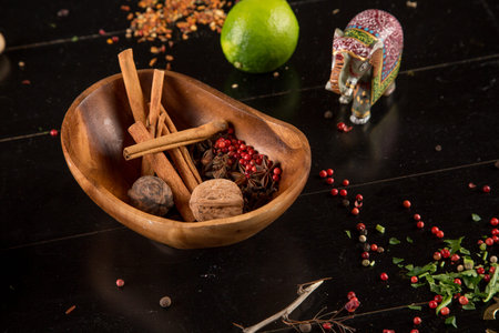 Cinnamon sticks and red pepper lie in a wooden bowl on a black table.
