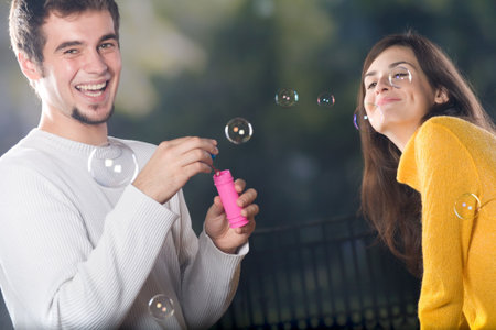 Young smiling couple blowing bubbles outdoors, funny 