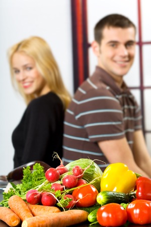 Vegetables on the table and blurred young happy smiling couple on backgroundの写真素材