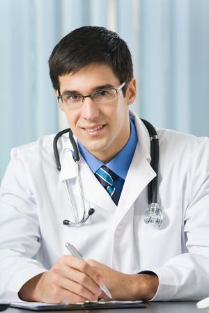 Happy doctor with stethoscope writing at officeの写真素材