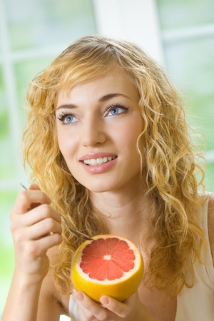 Young woman eating grapefruit at homeの写真素材