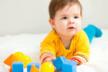 Happy baby girl playing with multicolored toys on bedの写真素材
