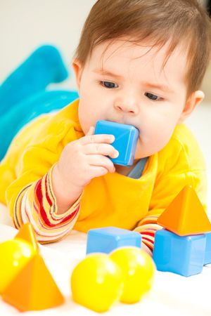 Happy baby girl playing with multicolored toys on bedの写真素材