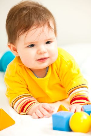 Happy baby girl playing with multicolored toys on bedの写真素材