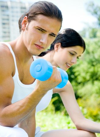 Young happy couple exercising with dumbbell, outdoors. Focus on manの写真素材