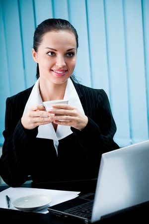 Portrait of businesswoman with coffee and laptop at officeの写真素材