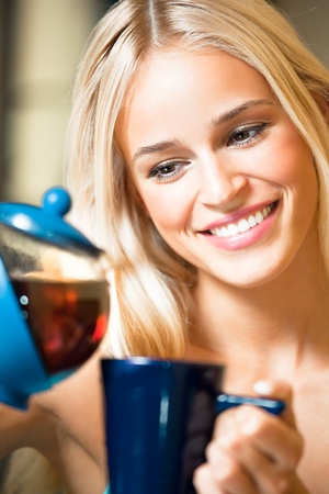 Portrait of young happy smiling woman with teapot and cup, indoorsの写真素材