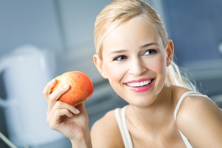 Portrait of young happy smiling woman with apple at homeの写真素材