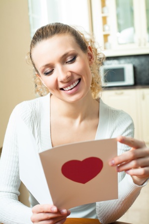 Young happy smiling woman, reading valentine card at homeの写真素材