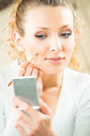 Young woman with mirror and makeup brush indoorsの写真素材