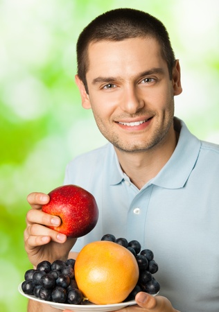 Portrait of young happy smiling man with plate of fruits, outdoorsの写真素材