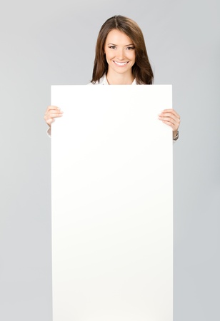 Happy smiling young business woman showing blank signboard, over grey backgroundの写真素材