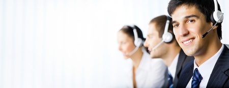 Three happy smiling young customer support phone operators at workplace. You can use left part for slogan, big text or banner.の写真素材