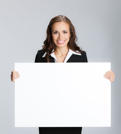 Happy smiling young business woman showing blank signboard, over grey backgroundの写真素材