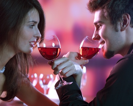 Young happy amorous couple with glasses of redwine on romantic date at restaurantの写真素材