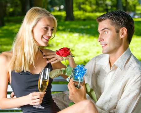 Young happy smiling cheerful attractive couple celebrating with glasses of champagne and rose,...