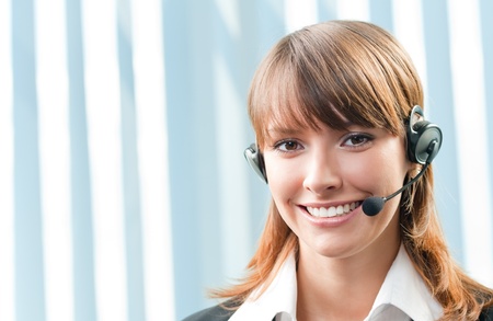 Young cheerful smiling support phone female operator in headset at office, with copyspaceの写真素材