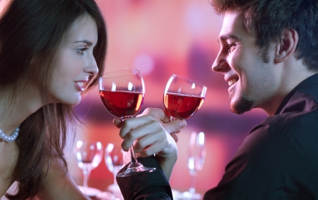 Young happy amorous couple with glasses of redwine on romantic date at restaurantの写真素材