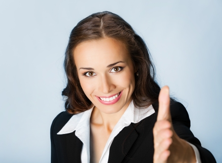 Portrait of young cheerful beautiful business woman giving hand for handshake, over blue backgroundの写真素材