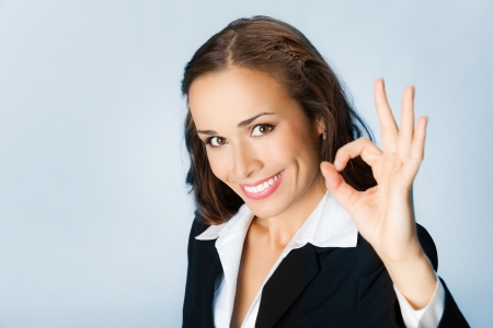 Happy smiling cheerful young business woman with okay gesture, over blue backgroundの写真素材